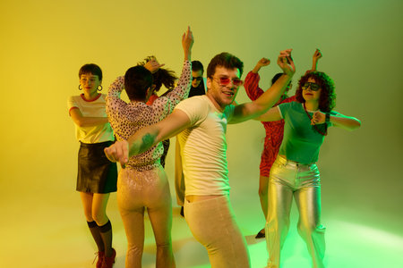 Smiling man in yellow shirt leading retro dance group under neon. Concept of individuality,...
