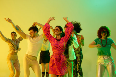 Smiling woman in pink dress dancing with group under neon yellow. Concept of joyful nightlife, retro...