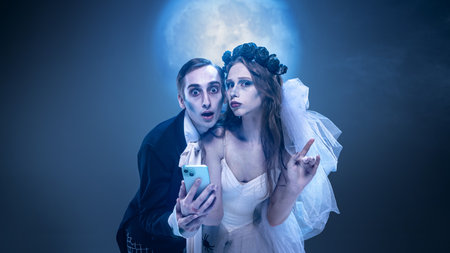 Surreal gothic couple with smartphone under moonlight in theatrical costume spooky portrait. Concept...