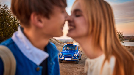Romantic couple smiling close to each other with retro blue car in background. Concept of love,...