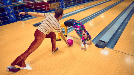 Man and woman performing playful acrobatics on bowling lane with retro outfits. Concept of humor in...