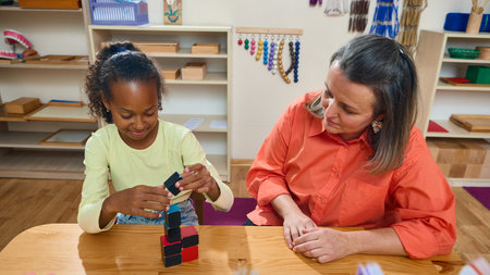Child stacking educational cubes under psychologist supervision. Concept of therapy, learning,...