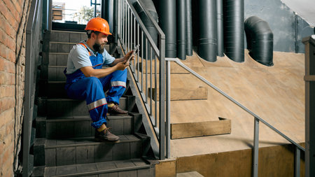 Technician using tablet on industrial staircase during break. Concept of HR and recruitment, modern...