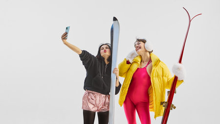 Two stylish women taking selfie in ski outfits with bright emotion. Concept of social connection, digital lifestyle, and winter joy for fashion, advertising, and influencer content.の写真素材