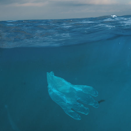 Plastic glove floating underwater representing ocean contamination. Concept of pollution, environmental protection, sustainability for awareness campaigns, education, and NGO visuals.の写真素材