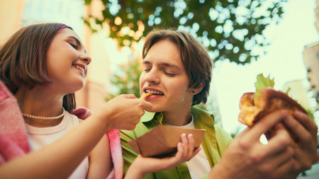Young woman feeding fry to cheerful man smiling together outdoors. Concept of emotional...