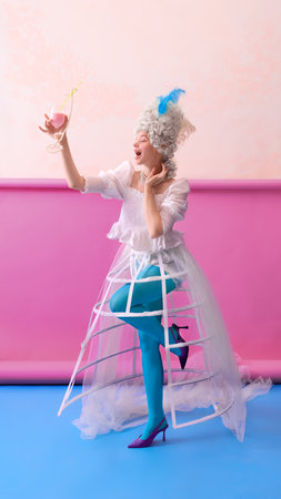 Joyful woman as Marie Antoinette raising glass with pearls against pink wall in celebration pose. Concept of luxury beverage and dessert campaign, cinematic storytelling, and lifestyle branding.の写真素材