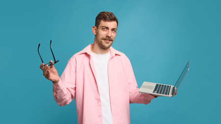 Confused man holding laptop and glasses expressing doubt and hesitation. Concept of UX testing, problem-solving ads, digital marketing, and emotional content for social media campaigns.の写真素材
