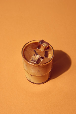 Iced coffee with milk and ice cubes in glass on warm beige background under natural light. Concept of beverage composition, lifestyle branding, cafe advertising, and editorial design.の写真素材