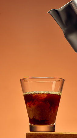 Coffee in glass with rich swirl texture and metal pitcher above against warm background. Concept of...