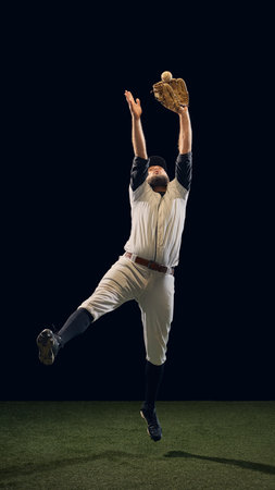 Baseball player jumping with glove raised to catch ball on dark background. Concept of athletic reach, reaction timing, and sports education for skill development.の写真素材