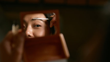 Woman applying eyebrow gel in mirror with precise calm focus. Concept of beauty precision, confidence, and mindful grooming in morning personal care routine.の写真素材