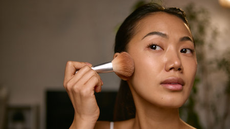 Woman applying blush with brush focusing on natural glow and tone. Concept of beauty enhancement, personal confidence, and balance between precision and self-expression.の写真素材