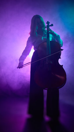 Female cellist standing and playing under purple studio lighting. Concept of music industry visuals, art and graphic design applications, and education materials for music schools.の写真素材