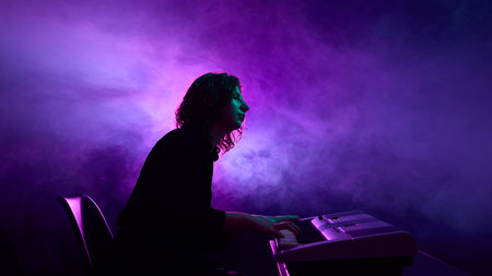 Pianist sitting at electronic keyboard surrounded by purple smoke. Concept of music industry promotion, musicians and clubs, and visual branding for modern campaigns.の写真素材