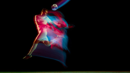 Soccer player striking airborne ball with red and blue neon motion trail. Concept of energy,...