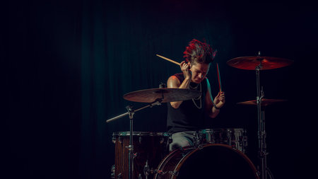 Young drummer focused on rhythm during rehearsal in dark studio light. Concept of motivation,...