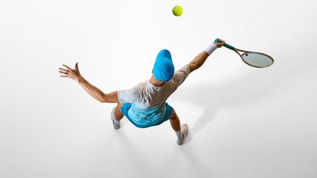 Male tennis player in blue outfit serving ball from overhead perspective on white background. Concept of sports marketing, body in motion, power performance.の写真素材