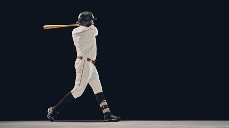 Baseball player completing full swing with wooden bat on dark background. Concept of motion analysis, sports technique, and athletic skill development for coaching and media use.の写真素材