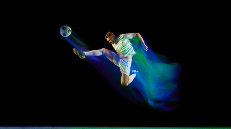 Soccer player performing midair kick surrounded by glowing blue and green light motion. Concept of ambition, focus, and physical excellence.の写真素材