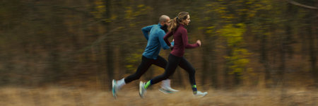 Wide panoramic view of runners sprinting through blurred autumn forest. Concept of outdoor speed, athletic drive, seasonal activity, fitness motivation and nature-based wellness routines. Bannerの写真素材