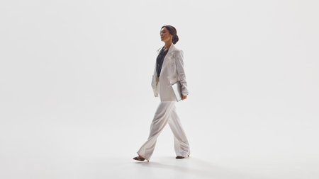 Stylish woman in white suit walking confidently representing success and power in modern fashion. Concept of luxury business aesthetics, empowerment, elegance for editorial and lifestyle use.の写真素材