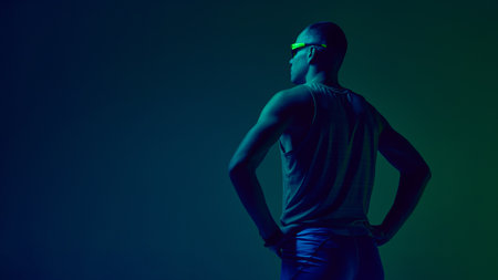 Athlete standing hands on hips in blue-green neon studio lighting. Concept of sports motivation visuals, trainer profile design, fitness challenge promos, athleticwear showcases.の写真素材