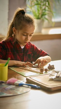 Girl focused on shaping clay during warm sunlit craft session. Concept of hands-on creativity, childhood learning, artistic exploration, and calm concentration in a cozy environment.の写真素材