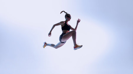 Futuristic athlete in dynamic mid-air leap against gradient light. Concept of high-performance training, agility drills, and modern fitness visuals with energized motion.の写真素材