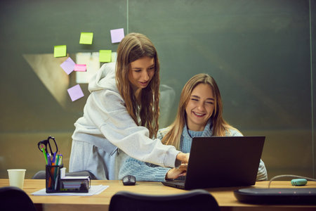Two young women studying together with laptop in friendly classroom mood. Concept of education content, teamwork visuals, learning materials, and school lifestyle storytelling.の写真素材