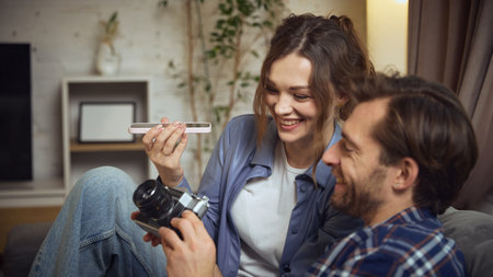 Couple laughing while checking vintage camera. Concept of bonding moments, shared hobbies, creative exploration, warm relationship mood at home.の写真素材