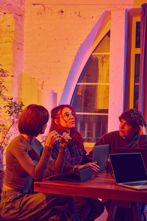 Focused coworking group discussing tasks with laptops and tablets. Concept of digital cooperation, workspace culture, project communication, and shared team alignment.の写真素材