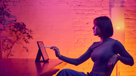 Woman pointing at tablet screen with stylus in neon workspace. Concept of digital design workflow,...