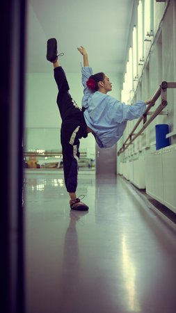 Ballerina stretching at barre during backstage warmup ritual. Concept of flexibility training,...