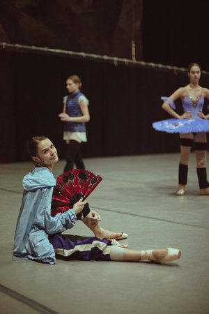Ballet dancer sitting on floor holding decorative fan during break. Concept of rehearsal pacing, performing arts education, backstage storytelling and dance lifestyle content.の写真素材