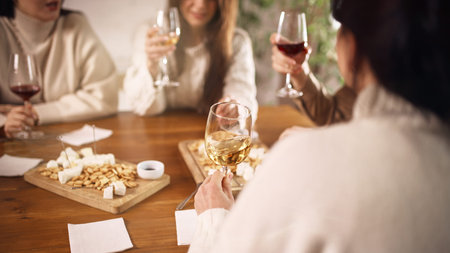 Group of friends tasting white wine at table with snacks indoors. Concept of casual social gathering, home hospitality, lifestyle content, and alcohol.の写真素材