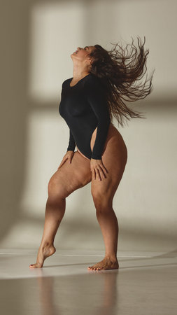 Curvy female model posing confidently in black bodysuit in studio. Concept of modern femininity, diversity representation, real body visibility, social awareness campaigns and editorial storytelling.の写真素材
