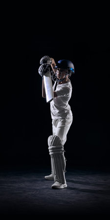 Junior cricket batsman holding bat in ready stance on black background. Concept of batting technique...