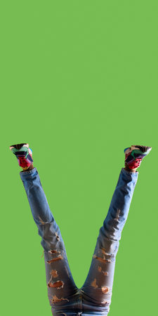 Female legs in ripped jeans and colorful sneakers on green background with copy space. Concept of streetwear trends, youth lifestyle marketing, sneaker banners, and vibrant minimal pop design.の写真素材