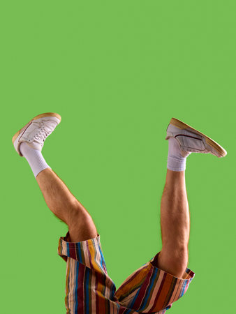 Male legs in white sneakers and striped shorts raised against green background. Concept of mens fashion catalog cover, online store image, casual outfit presentation and digital advertising mockup.の写真素材