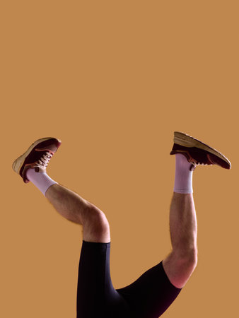 Male legs in brown sneakers and white socks bent on beige background. Concept of mens footwear promotion, everyday outfit campaign, ecommerce product display and retail advertising use.の写真素材
