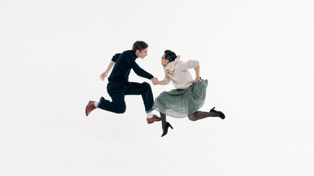 Man and woman suspended in jump facing each other and holding hands on white studio background....