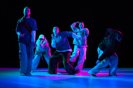 Hip hop dancers performing street dance choreography under neon lighting for music advertising,...