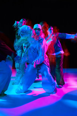 Hip hop dancers performing synchronized street dance under colorful neon lighting with motion blur.