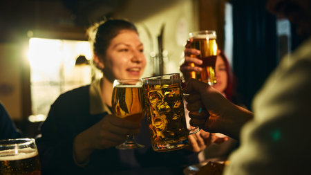 Close up beer toast between friends in pub during casual night out, social drinking and lively bar atmosphere.の写真素材