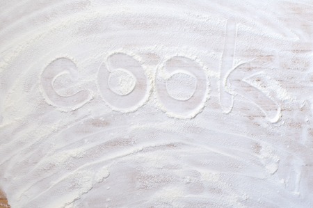 Word cook on wood board with flour on wooden tableの写真素材