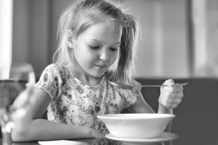 Cute little girl eating a soup in the restaurant. Black and white photoの写真素材