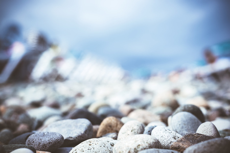 Blurred background of the close up stony on beach on the Black Sea coast with plastic sunbeds, blue...