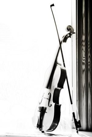 Vertical image of a violin with sheet music  the front of the fiddle on windows background. Black and white photo.の写真素材