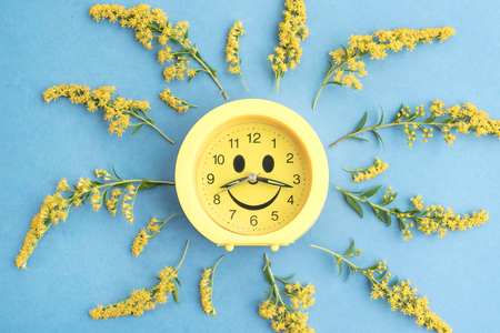 Clock watch with eyes and smile and summer yellow wild flowers on blue background. Springtime floral composition.  Flat lay, top view, copy space.の写真素材